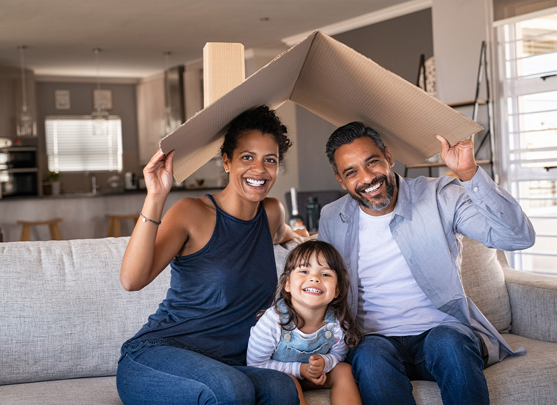 Insurance Solutions - Happy Family With Child Holding a Cardboard Roof in Their Living Room at Home